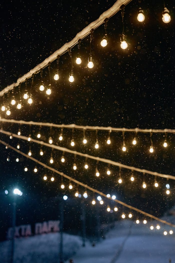 Warm glowing string lights illuminating a snowy evening ambiance, perfect for holiday themes.